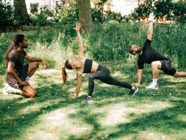Two people stretching outdoors with an instructor watching.