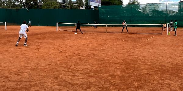 Four people playing doubles tennis on a clay court.