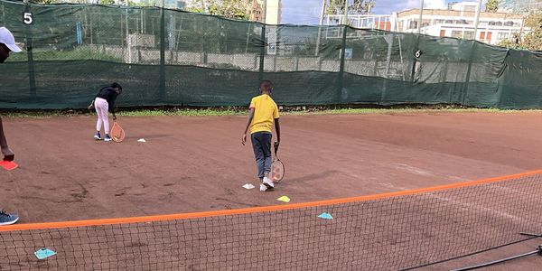 Children practicing tennis drills on a clay court with an instructor.