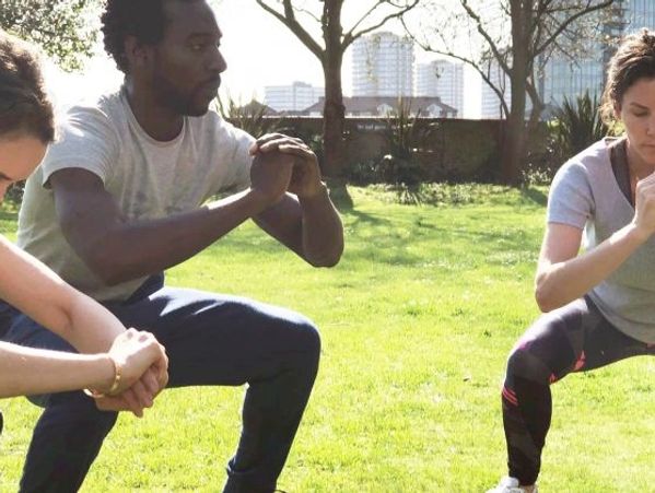 Three people exercising outdoors, doing squats in a park.