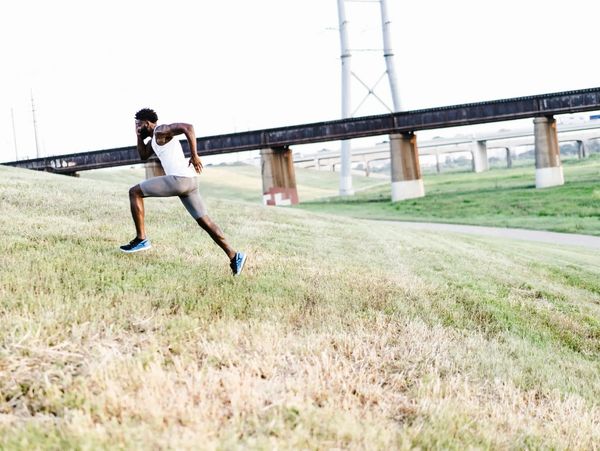 Man sprinting uphill in athletic wear near a bridge.