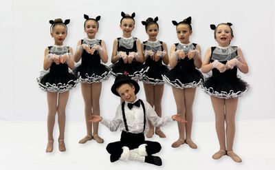 A group of children in black and white dance costumes posing with a boy in suspenders.