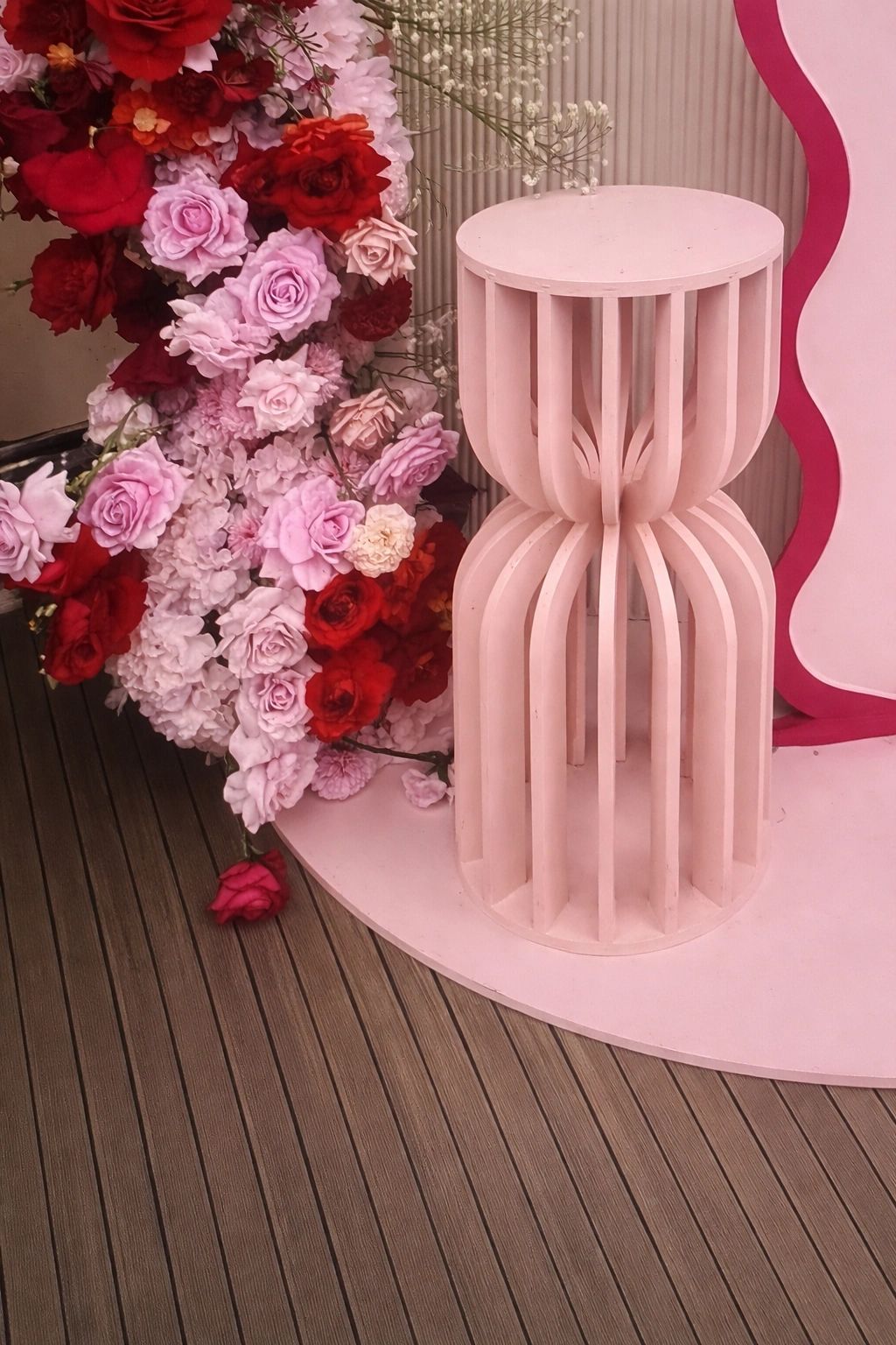 Pink decorative stool beside a vibrant floral arrangement of red and pink roses.