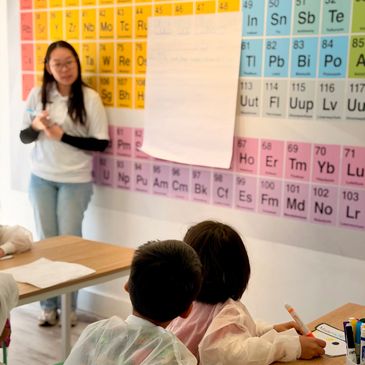 Teacher explaining chemistry to kids using a periodic table.