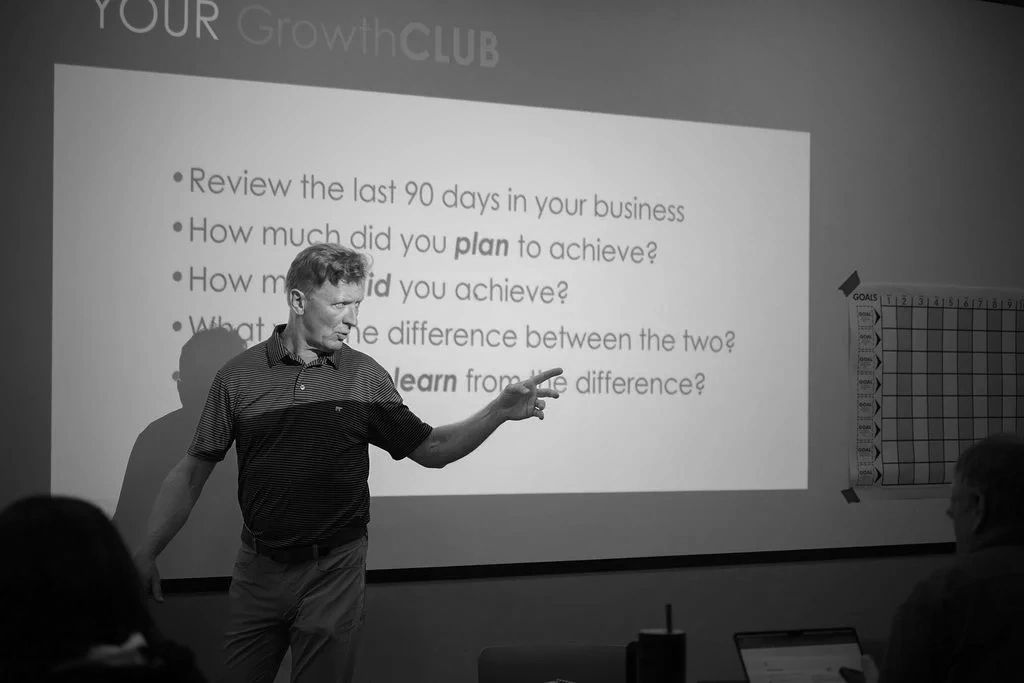 A man presenting business review questions to a small audience in a classroom.