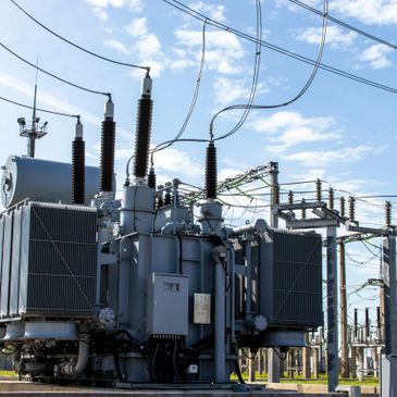 High-voltage electrical transformer in an outdoor substation under a blue sky.