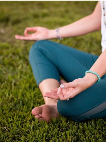 Person meditating outdoors in a cross-legged position on grass.
