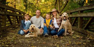 A happy family with two dogs sitting on a leaf-covered bridge in autumn.