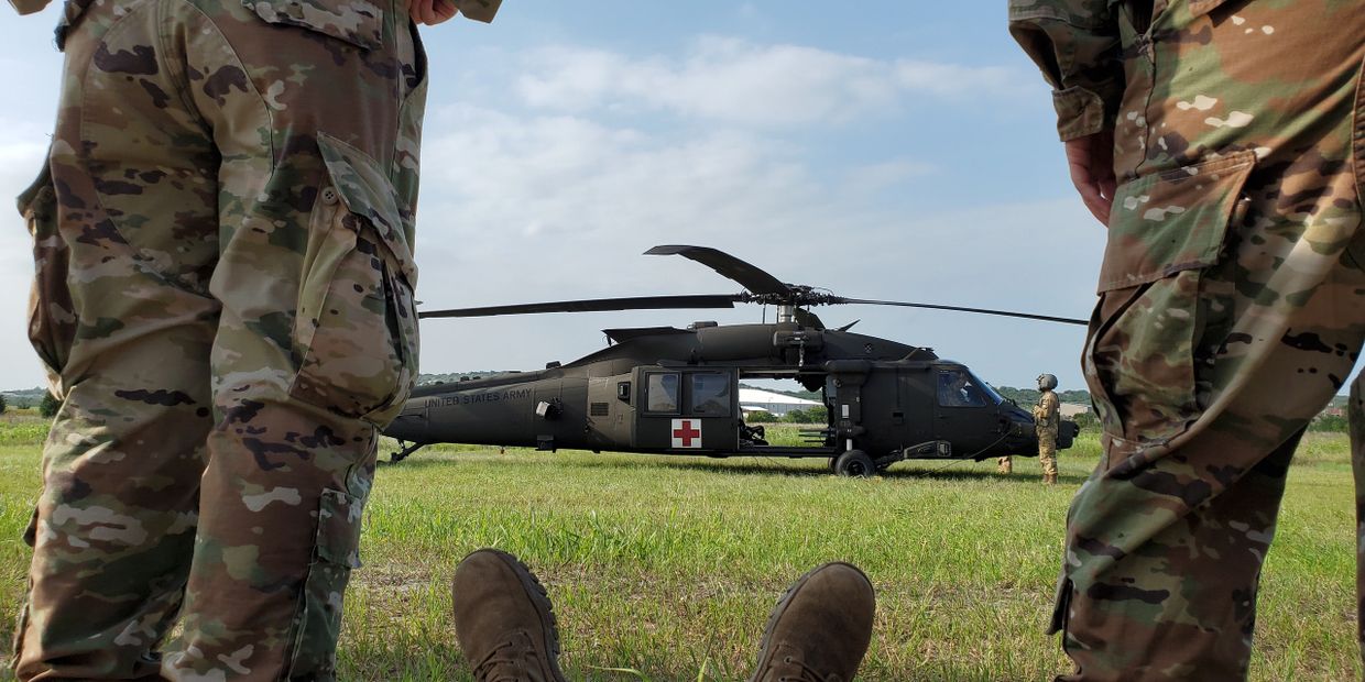 Military medics stand by a medical helicopter on a grassy field.