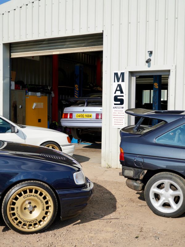 Several classic cars parked outside and inside a garage.