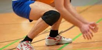 Athlete wearing knee pads preparing to receive a volleyball indoors.