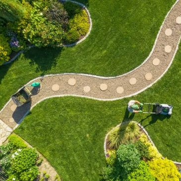 A person mowing a lush green lawn with landscaped garden beds.
