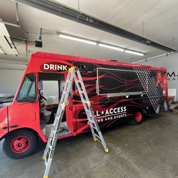 Red and black branded event truck with a ladder in front inside a garage.