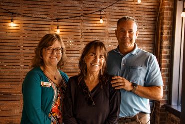 Three adults smiling and posing in a warmly lit rustic room.
