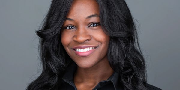 Confident woman with long black hair smiling against a gray background.