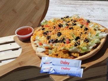 Loaded taco salad pizza with sauce and condiments.