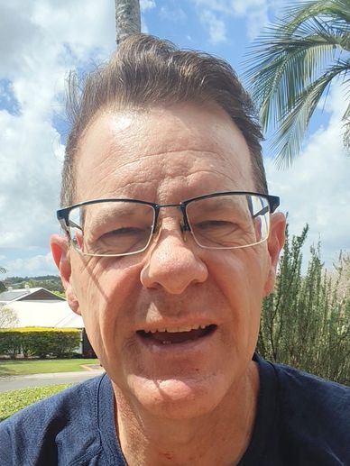 Smiling man wearing glasses outdoors under a blue sky.