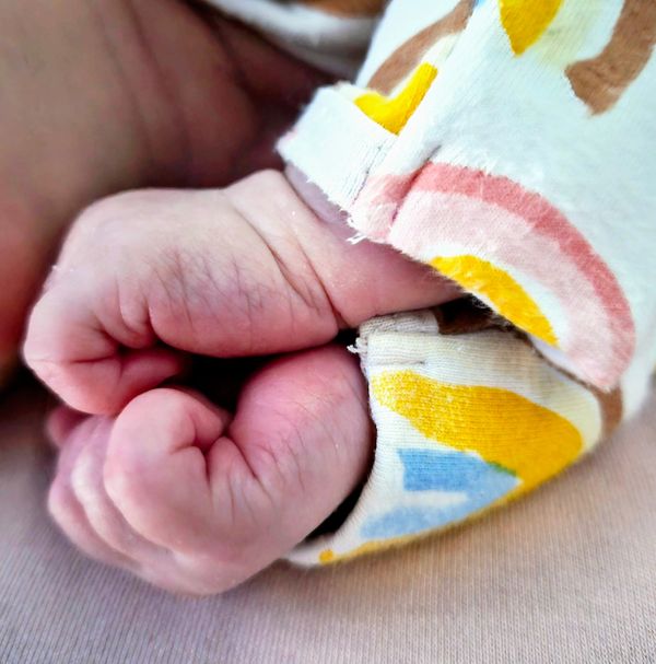 Close-up of a newborn baby's tiny clenched fists wrapped in colorful fabric.