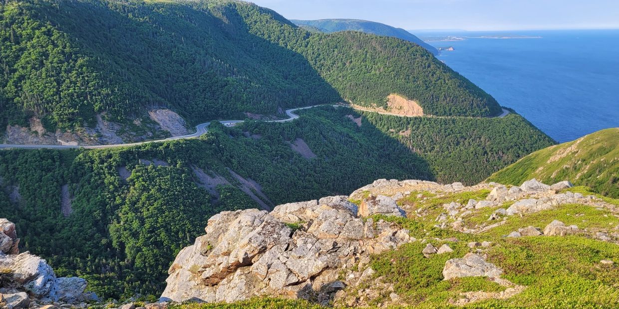Scenic mountain road winding through lush green hills by the ocean.