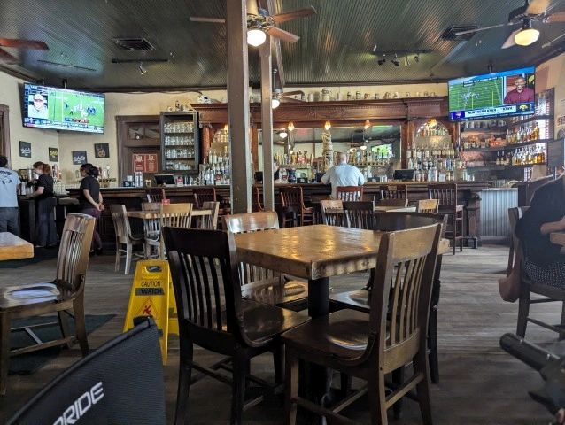 Empty wooden tables and chairs in a cozy bar with TV screens.