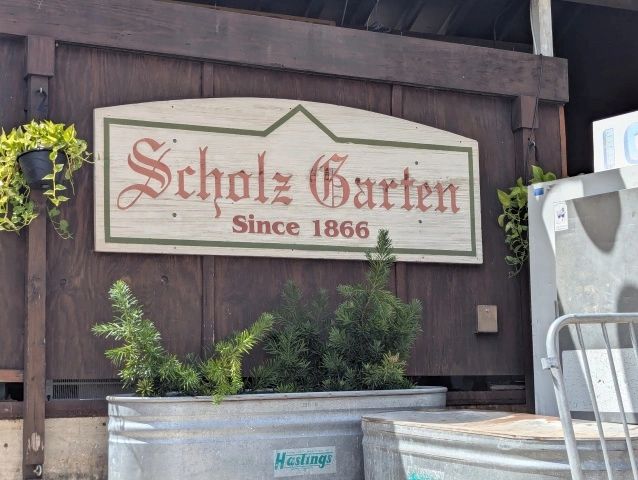 Sign reading "Scholz Garten Since 1866" above plants.
