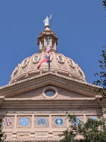 Dome of a historical building with flags and a statue on top.