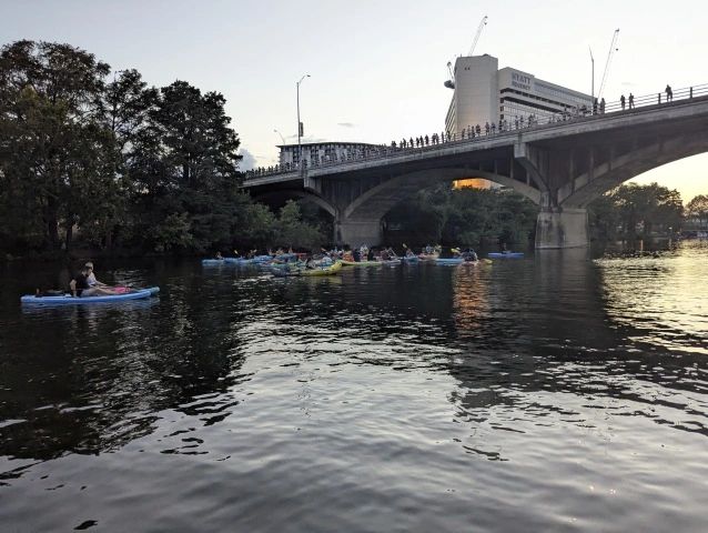 Kayakers paddling under a bridge at dusk.