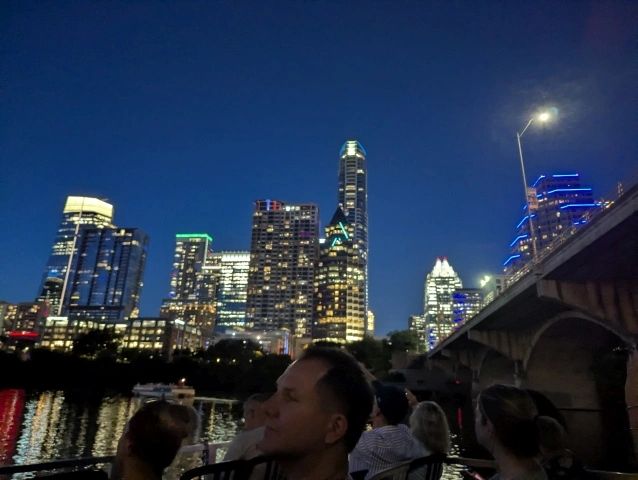 People enjoy a nighttime city skyline from a waterfront.