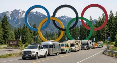 Vehicles parked under large Olympic rings in a mountainous area.