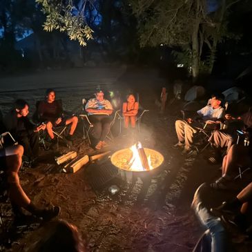 Group of people sitting around a campfire at night in the woods.