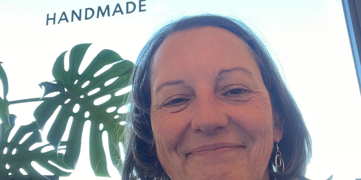 Smiling woman with earrings near a plant and handmade sign.