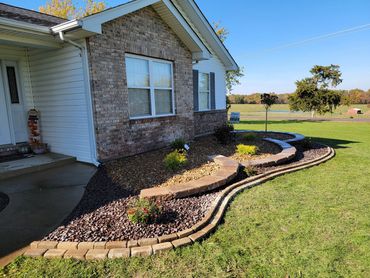 A landscaped garden bed with decorative stones and plants in front of a house.