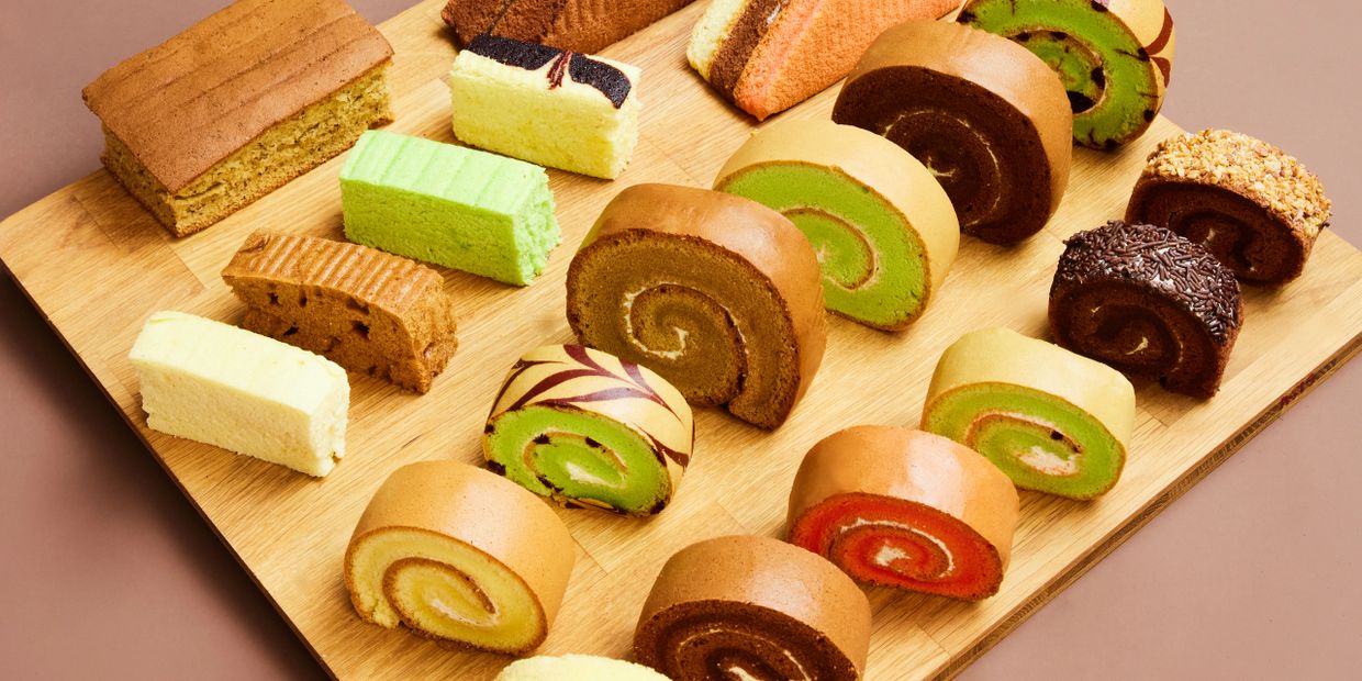 Assorted colorful Swiss roll cakes and sponge cakes arranged on a wooden board.
