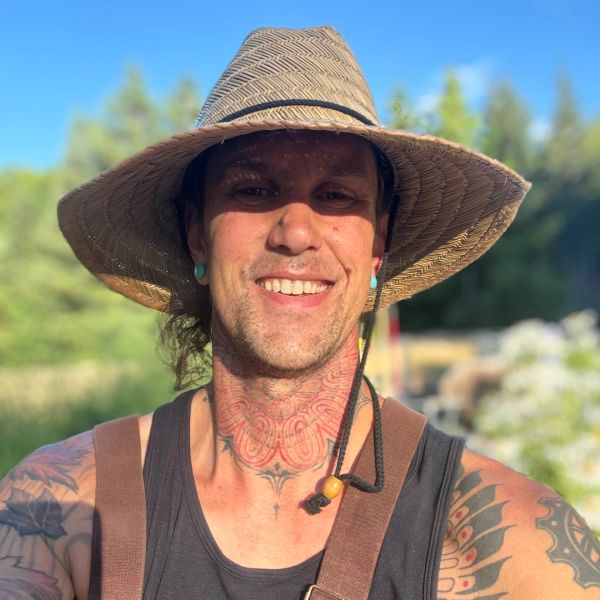 Smiling man wearing a wide-brimmed hat and showcasing colorful tattoos.