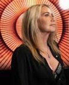 Woman with blonde hair poses in front of a vibrant circular art piece.
