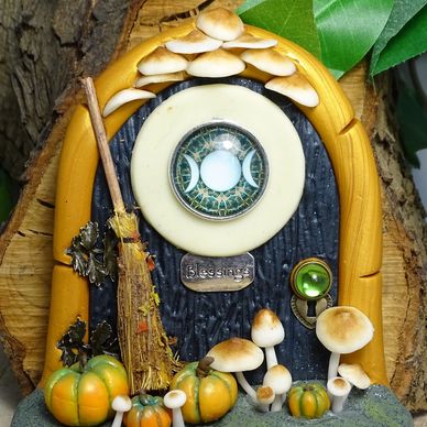 A whimsical miniature witch door with pumpkins, mushrooms, and a broomstick.