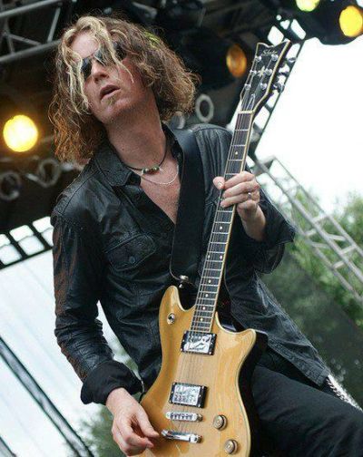 Rock guitarist performing on stage with blonde hair and sunglasses.
