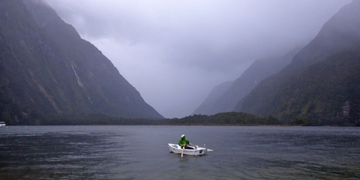 Person rowing a boat in a misty mountain lake.
