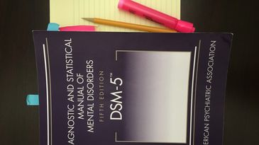 DSM-5 book with a notepad, pencil, and highlighter.