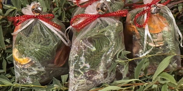 Three decorative sachets with greenery, dried fruit, and red bows.