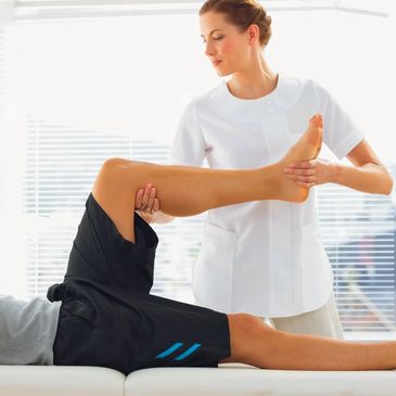 A man receives a sports massage on his bent leg, lying on his back with a therapist.