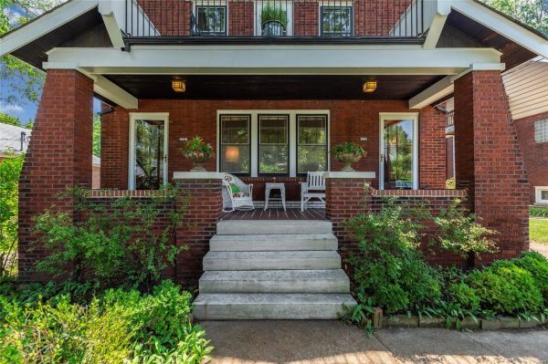 Cozy brick house porch with chairs and greenery.