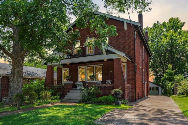 Two-story brick house with porch and large tree.