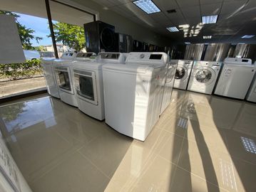 A showroom with various washing machines and dryers under bright lighting.