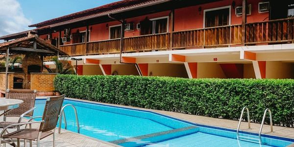 Outdoor swimming pool with chairs and a two-story building in the background.