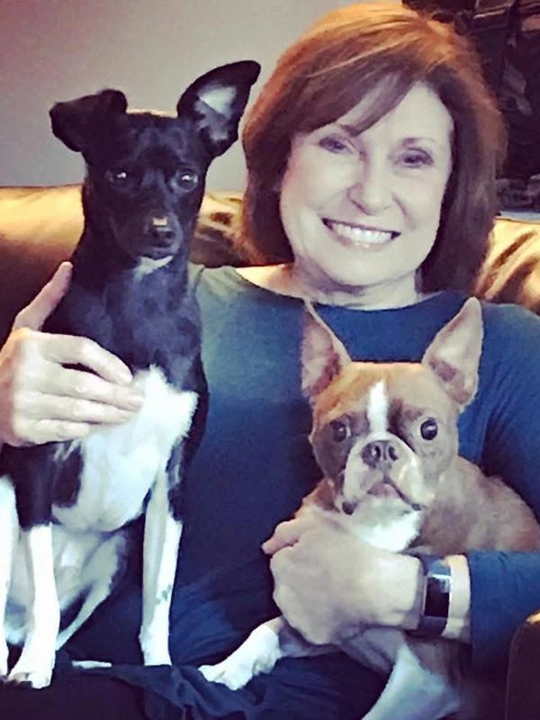A woman smiling with two dogs on a couch.