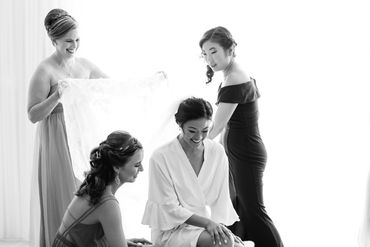 Bride surrounded by bridesmaids preparing with a veil in a bright room.