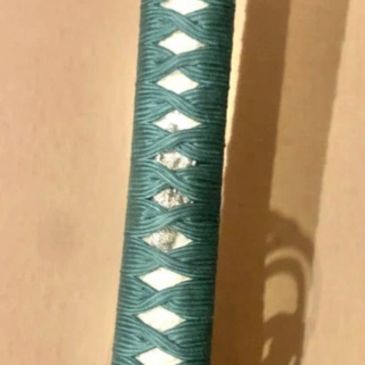 Close-up of a katana handle wrapped in teal cord.