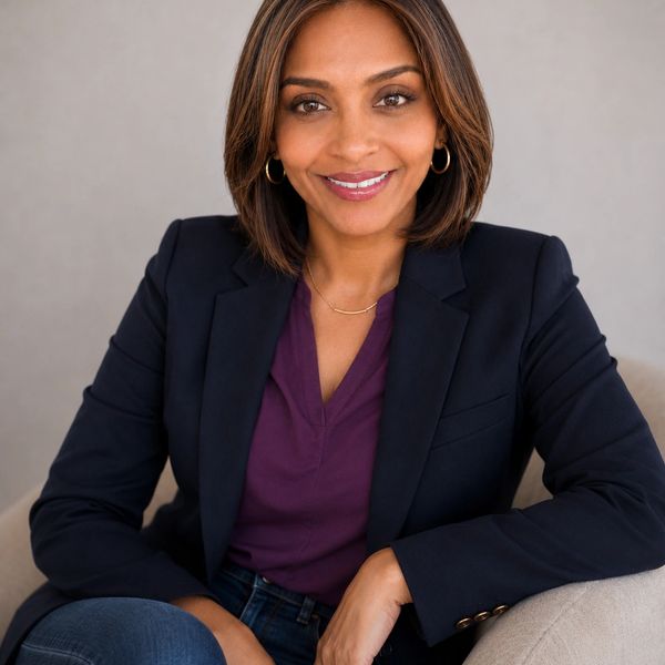 Confident woman in a blazer sitting and smiling at the camera.