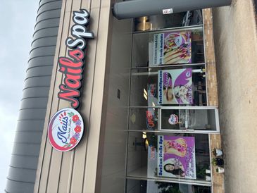 Nail spa storefront with promotional posters and open sign.